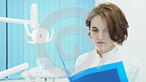 Woman doctor examines documents with patient`s tests. Media. Woman doctor in white coat on background of treatment room