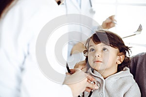 Woman-doctor examining a child patient by stethoscope. Cute arab toddler and his brother at physician appointment