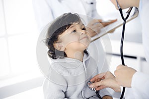 Woman-doctor examining a child patient by stethoscope. Cute arab toddler at physician appointment. Medicine concept