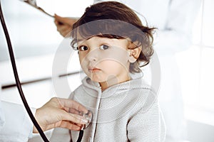 Woman-doctor examining a child patient by stethoscope. Cute arab toddler at physician appointment. Medicine concept