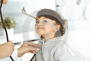 Woman-doctor examining a child patient by stethoscope. Cute arab toddler at physician appointment. Medicine concept