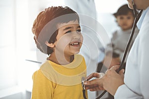 Woman-doctor examining a child patient by stethoscope in sunny clinik. Cute arab boy at physician appointment