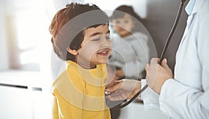 Woman-doctor examining a child patient by stethoscope in sunny clinik. Cute arab boy at physician appointment