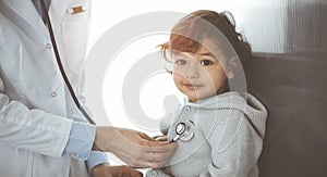 Woman-doctor examining a child patient by stethoscope in sunny clinik. Cute arab toddler at physician appointment