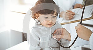 Woman-doctor examining a child patient by stethoscope in sunny clinik. Cute arab toddler at physician appointment