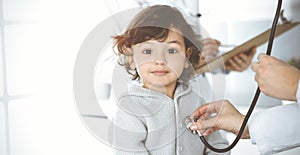 Woman-doctor examining a child patient by stethoscope in sunny clinik. Cute arab toddler at physician appointment