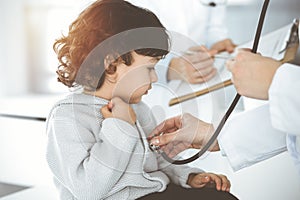 Woman-doctor examining a child patient by stethoscope in sunny clinik. Cute arab toddler at physician appointment