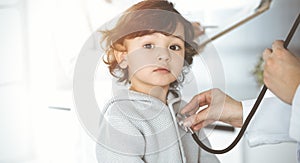 Woman-doctor examining a child patient by stethoscope in sunny clinik. Cute arab toddler at physician appointment