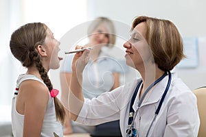 Woman doctor examining little girl mouth at office. Doctor at hospital checking the sore throat of a young patient