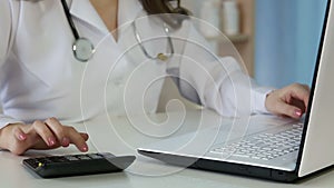 Woman doctor filling in health insurance form on laptop, calculating expenses
