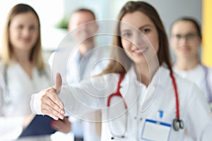 Woman doctor giving hand for handshake on background of colleagues in clinic closeup