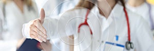 Woman doctor giving hand for handshake on background of colleagues in clinic closeup