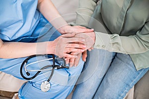 Woman doctor holding patient hands, caring elderly female at medical appointment