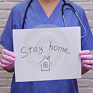 Woman doctor holding a poster calling to stay home. Nurse in protective gloves with a sheet in her hands