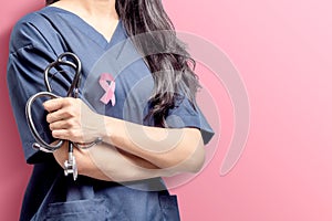 Woman doctor holding a stethoscope on her hands with pink ribbon over pink background