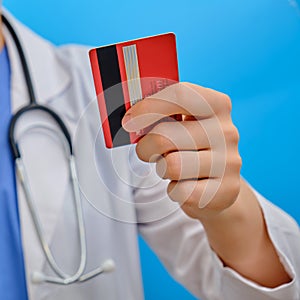 Woman doctor holds a credit card, close-up. A nurse in medical dress with a red plastic card on a blue background