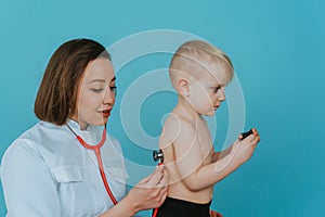 Woman doctor listens with a stethoscope to the lungs of a little boy