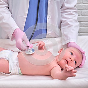 Woman doctor listens with a stethoscope to a newborn baby. Nurse checks the child health with a stethoscope