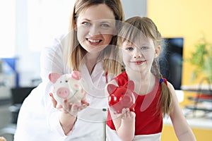 Woman doctor and little girl holding piggy banks