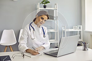 Woman doctor making notes during online lesson or video call consultation in medical clinic photo