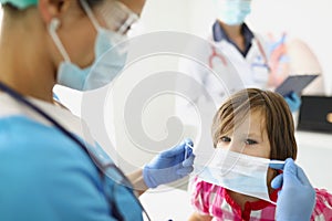 Woman doctor in a mask puts a mask on a child