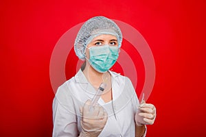 Woman doctor in medical clothes holds a syringe and an ampoule in her hands. Studio photo on a red background.