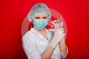 Woman doctor in medical clothes holds a syringe and an ampoule in her hands. Studio photo on a red background.