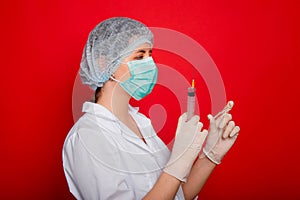 Woman doctor in medical clothes holds a syringe and an ampoule in her hands. Studio photo on a red background.