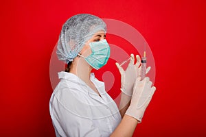 Woman doctor in medical clothes holds a syringe and an ampoule in her hands. Studio photo on a red background.