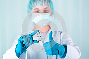 Woman doctor or nurse in uniform and gloves wearing face mask protective in lab holding medicine vial vaccine bottle with COVID-19