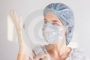 Woman doctor nurse wearing medical mask and hat, putting on disposable gloves. Protection from coronavirus infection, health care