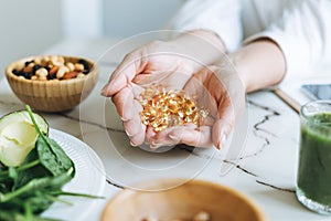 Woman doctor nutritionist hands in white shirt with omega 3, vitamin D capsules with green vegan food. The doctor prescribes a