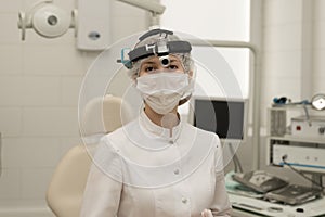 woman-doctor-otolaryngologist in a modern office ENT of the hospital, looks into the camera in a white coat and a mask