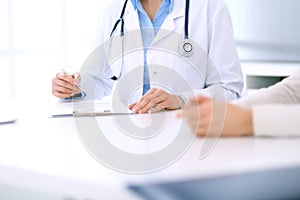 Woman doctor and patient sitting and talking at medical examination at hospital office, close-up. Physician filling up