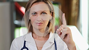Woman doctor pointing finger up in medical office photo