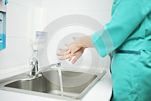 A woman doctor in protective mask washes hands thoroughly in hospital