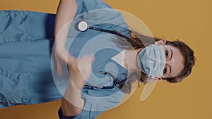 Woman doctor putting on covid mask for protection and posing confindent with arms crossed in studio