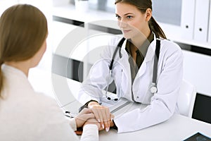 Woman doctor reassuring her female patient at hospital office. Medical ethics, human support and trust concept in