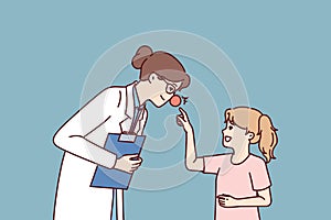 Woman doctor with red nose leans towards little girl for concept treating in pediatric clinic