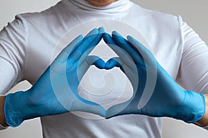 Woman doctor`s hands in blue gloves form a heart shape in home