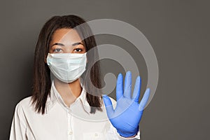 Woman doctor or scientist in a medical face mask showing stop pandemic gesture. Black woman in safety mask and medical gloves