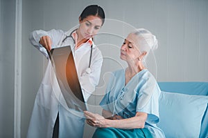 Woman doctor show x-ray film result and explain of health problem to elderly women patient at room in hospital. Healthcare