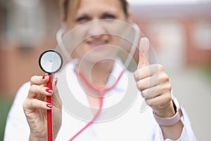 Woman doctor showing thumb up and head of stethoscope closeup