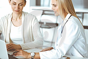Woman-doctor sitting and communicating with her female patient in clinic. Blonde physician happy to help. Medicine