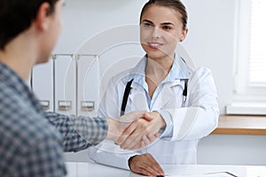 Woman-doctor smiling while shaking hands with her male patient. Medicine concept