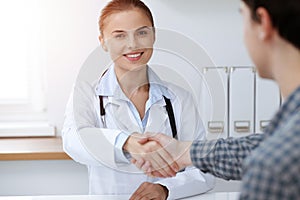 Woman-doctor smiling while shaking hands with her male patient. Medicine concept