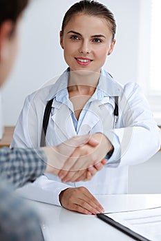 Woman-doctor smiling while shaking hands with her male patient. Medicine concept