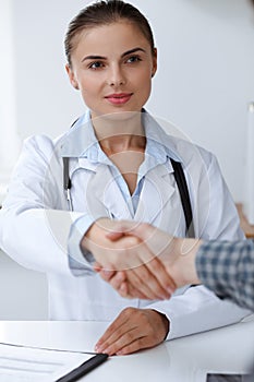 Woman-doctor smiling while shaking hands with her male patient. Medicine concept