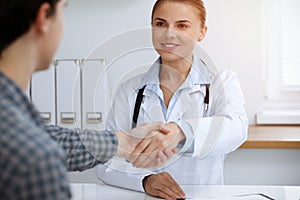 Woman-doctor smiling while shaking hands with her male patient. Medicine concept