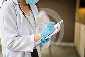 Woman doctor with stethoscope and blue glove write report by pencil in a paper at hospital